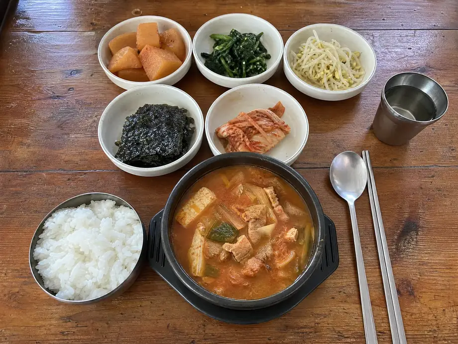 Korean baekban set meal with kimchi jjigae, rice, and multiple banchan side dishes on wooden table