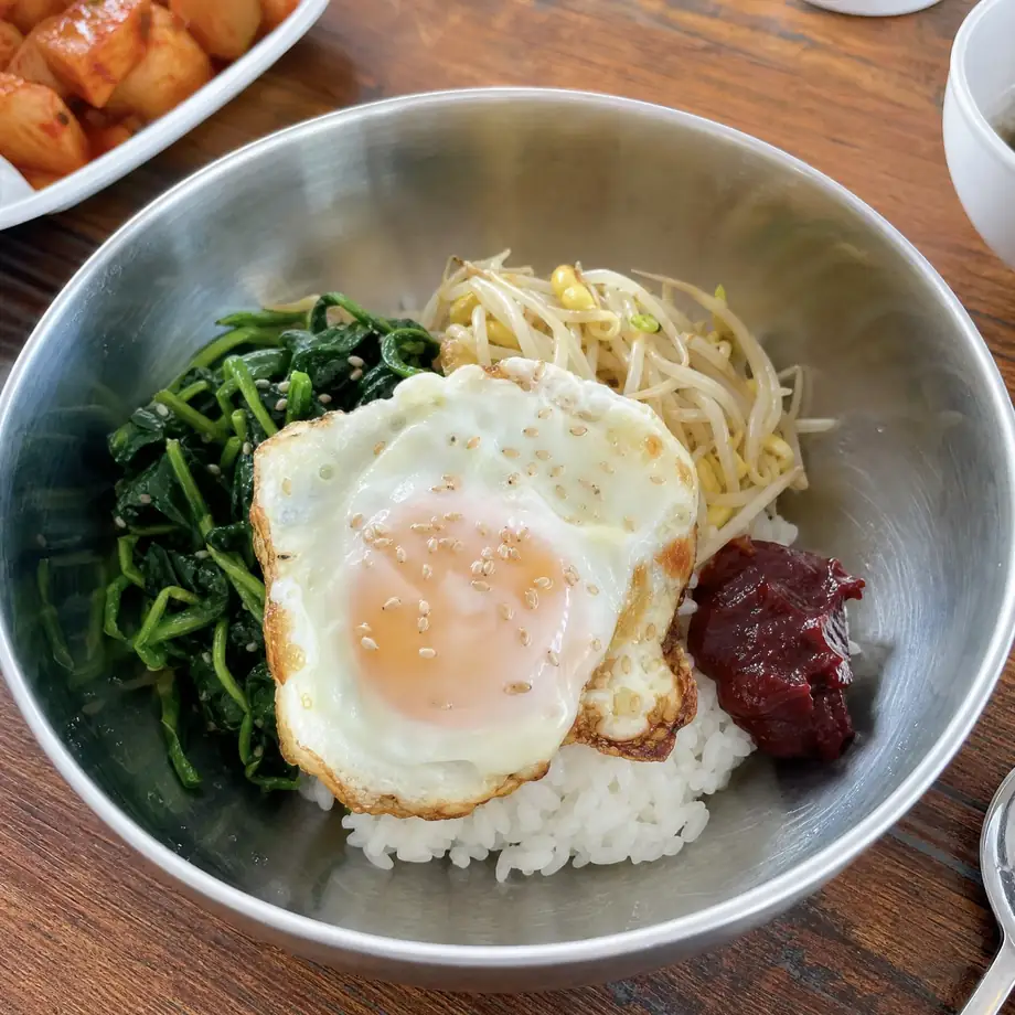 Simple homemade Korean bibimbap with fried egg, spinach namul, bean sprouts and gochujang in stainless bowl