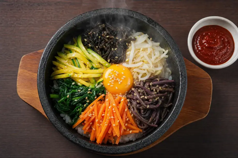 Dolsot bibimbap Korean mixed rice bowl in hot stone pot with colorful vegetables and egg yolk