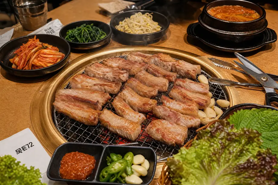 Korean BBQ samgyeopsal pork belly grilling on charcoal with banchan side dishes